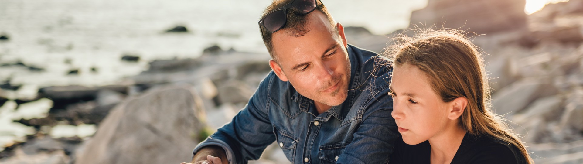 Man sitting with child on rocks by the ocean