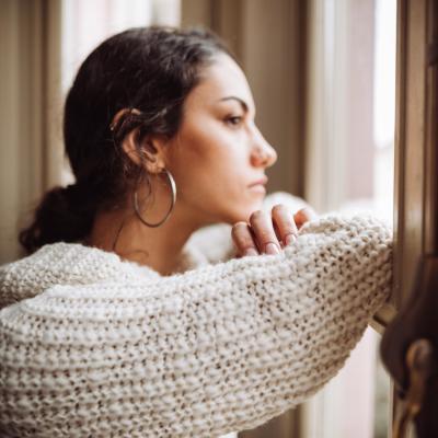 Profile view of a woman with long dark hair wearing large hooped earrings and a woolly jumper looking out a window